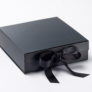 May include: A black gift box with a matching black ribbon tied in a bow. The box is rectangular with a glossy finish. The ribbon is made of a satin-like material. The box is closed and ready for gifting.