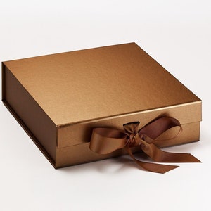 May include: A rectangular, bronze-colored gift box with a matching ribbon tied in a bow. The box has a matte finish and a magnetic closure. The ribbon is a darker shade of brown.