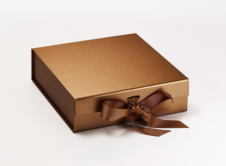 May include: A rectangular, bronze-colored gift box with a matching ribbon tied in a bow. The box has a matte finish and a magnetic closure. The ribbon is a darker shade of brown.
