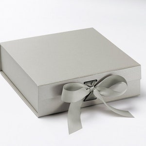 May include: A rectangular, light gray gift box with a matching satin ribbon tied in a bow. The box has a magnetic closure and a textured surface, perfect for presenting gifts or storing keepsakes.