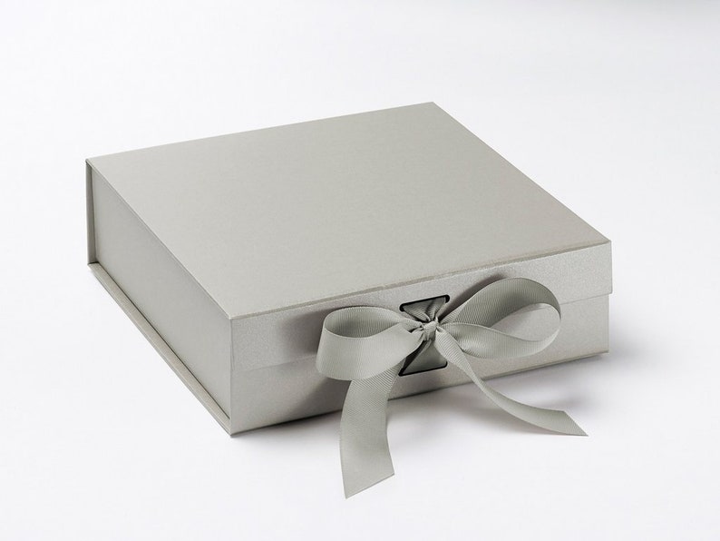 May include: A rectangular, light gray gift box with a matching satin ribbon tied in a bow. The box has a magnetic closure and a textured surface, perfect for presenting gifts or storing keepsakes.