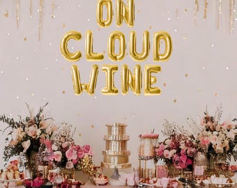 May include: A pink table setting with gold balloons spelling "On Cloud Wine". The table is decorated with flowers, candles, and other party decorations.