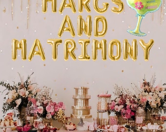 May include: Gold foil balloons spelling "MARGS AND MATRIMONY" with a gold and green margarita balloon. A table is set with pink and white flowers, a tiered cake stand, and other decorations.