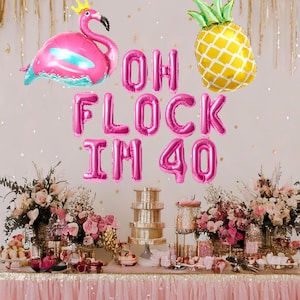 May include: Pink and gold foil balloons spelling "Oh Flock I'm 40" with a pink flamingo and a pineapple balloon. The balloons are decorated on a table with pink and gold decorations.