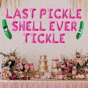 May include: Pink foil balloons spelling "Last Pickle Shell Ever Tickle" with green pickle balloon decorations on either side. A table is set with pink and gold decorations and a tiered cake stand.
