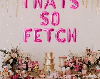 May include: Pink balloon letters spelling "That's So Fetch" on a white wall with pink confetti. A table with pink and gold decorations and a pink tablecloth is in the foreground.