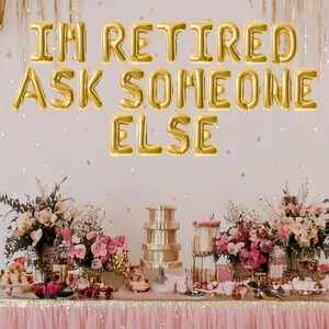 May include: A pink and gold party table decorated with flowers and balloons. The balloons spell out "I'm Retired Ask Someone Else".