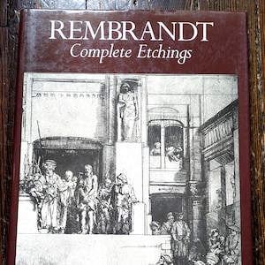 Op de afbeelding: Een hardcover boek getiteld "REMBRANDT Complete Etchings" met een donkerrode kaft. De kaft toont een gedetailleerde zwart-wit ets van een historische scène met figuren in kleding uit die tijd, tegen een architecturale achtergrond.