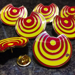 May include: Six yellow and red enamel pins with a concentric circle design. The pins are in the shape of a crescent moon.
