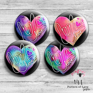 May include: Four round buttons with a black background and a white outline of the American Sign Language symbol for "love" inside a heart shape. The hearts are filled with watercolor-like designs in shades of pink, purple, blue, and green.
