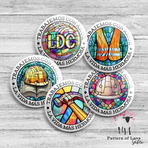 May include: Five round, silver-colored, decorative metal discs with stained glass designs. Each disc features a different image, including a hard hat, a book, a hammer, a safety vest, and the letters "LDC". The text "Trabajemos con amor la vida mas hermosa" is written around the edge of each disc.