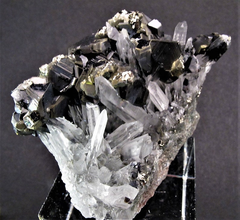 May include: A cluster of black and silver crystals with a clear quartz matrix. The crystals are sharp and well-defined, and the matrix is smooth and polished.