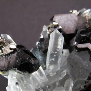 May include: A cluster of black and silver crystals with clear quartz crystals. The crystals are arranged in a natural formation.