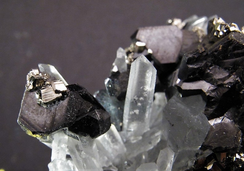 May include: A cluster of black and silver crystals with clear quartz crystals. The crystals are arranged in a natural formation.