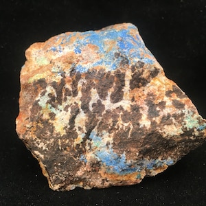 May include: A rough, irregularly shaped rock with a mix of brown, white, blue, and green colors. The rock has a mottled appearance with patches of different colors.