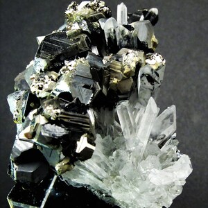 May include: A cluster of black, silver, and gold crystals on a black background. The crystals are arranged in a random pattern and are of varying sizes. The crystals are sharp and have a metallic sheen.