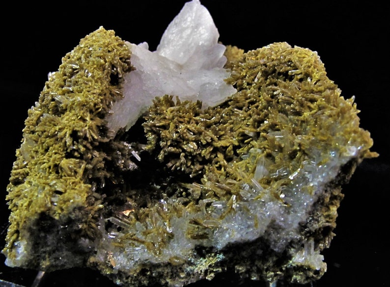 May include: A cluster of clear quartz crystals with a green mineral, possibly actinolite, growing on the surface. The quartz crystals are clear and have a glassy lustre. The actinolite is a dark green colour and has a fibrous texture.