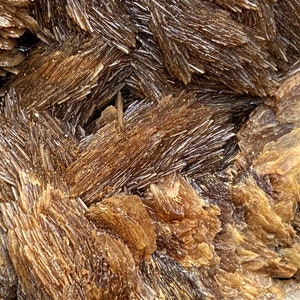 May include: Close-up of a brown, crystalline mineral with a layered, striated texture. The mineral has a shiny, reflective surface.