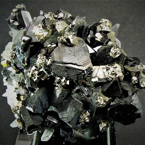 May include: A cluster of black, metallic, and shiny crystals with a silvery, metallic mineral. The crystals are arranged in a random pattern and are surrounded by a white, translucent mineral.