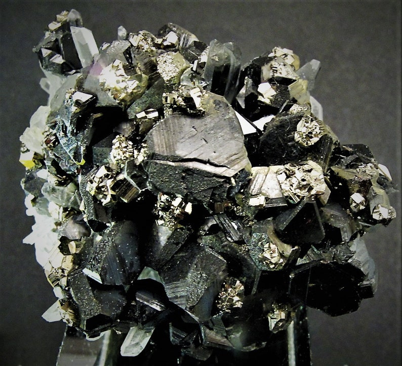 May include: A cluster of black, metallic, and shiny crystals with a silvery, metallic mineral. The crystals are arranged in a random pattern and are surrounded by a white, translucent mineral.