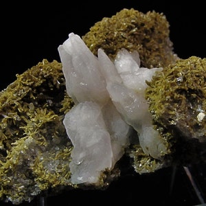 May include: A cluster of translucent, pale pink quartz crystals surrounded by a bed of green, mossy-looking crystals.