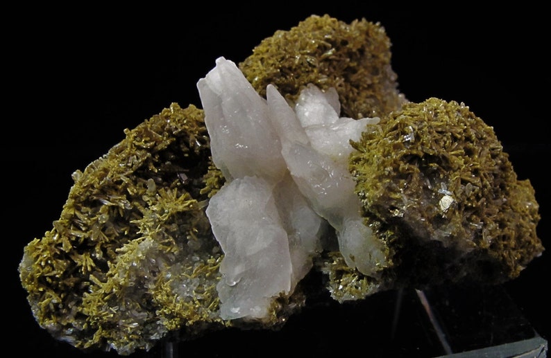 May include: A cluster of translucent, pale pink quartz crystals surrounded by a bed of green, mossy-looking crystals.