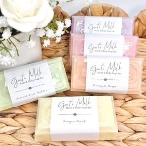 Puede incluir: Cuatro jabones rectangulares de leche de cabra para manos y cuerpo en colores verde claro, melocot&oacute;n, rosa y lavanda. Cada barra tiene una etiqueta de papel blanco con el texto Goat's Milk Hand & Body Soap Bar y nombres de aromas como Coconut Lime Verbena, Pineapple Mango y Georgia Peach.