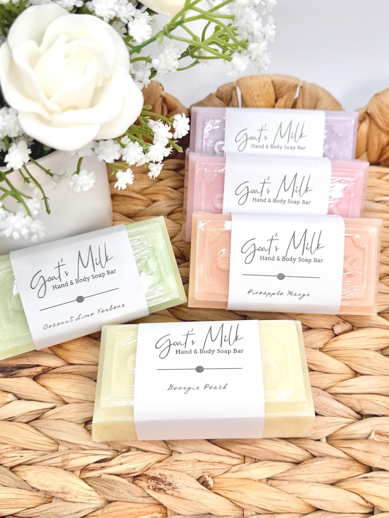 Puede incluir: Cuatro jabones rectangulares de leche de cabra para manos y cuerpo en colores verde claro, melocot&oacute;n, rosa y lavanda. Cada barra tiene una etiqueta de papel blanco con el texto Goat's Milk Hand & Body Soap Bar y nombres de aromas como Coconut Lime Verbena, Pineapple Mango y Georgia Peach.