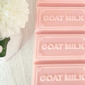 Puede incluir: Una pastilla de jab&oacute;n rectangular de color rosa dividida en cuatro segmentos, cada uno con el texto GOAT MILK grabado en letras may&uacute;sculas. El jab&oacute;n presenta un borde decorativo alrededor de cada secci&oacute;n y tiene un acabado liso y s&oacute;lido.
