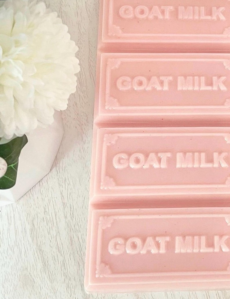 Puede incluir: Una pastilla de jab&oacute;n rectangular de color rosa dividida en cuatro segmentos, cada uno con el texto GOAT MILK grabado en letras may&uacute;sculas. El jab&oacute;n presenta un borde decorativo alrededor de cada secci&oacute;n y tiene un acabado liso y s&oacute;lido.