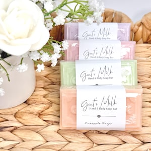 Puede incluir: Una pila de cuatro pastillas de jab&oacute;n rectangulares de leche de cabra para manos y cuerpo en tonos pastel morado, rosa, verde y naranja. Cada pastilla tiene una etiqueta de papel blanco con el texto Goat's Milk Hand & Body Soap Bar, y la inferior indica Pineapple Mango.