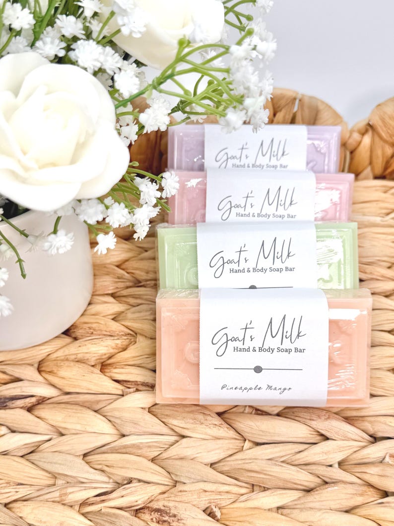 Puede incluir: Una pila de cuatro pastillas de jab&oacute;n rectangulares de leche de cabra para manos y cuerpo en tonos pastel morado, rosa, verde y naranja. Cada pastilla tiene una etiqueta de papel blanco con el texto Goat's Milk Hand & Body Soap Bar, y la inferior indica Pineapple Mango.