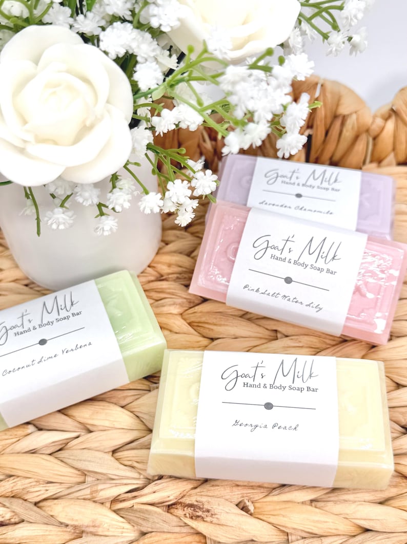 Puede incluir: Cuatro pastillas de jab&oacute;n de leche de cabra para manos y cuerpo en colores verde claro, amarillo, rosa y lavanda. Cada pastilla tiene una etiqueta de papel blanco con el texto Goat's Milk Hand & Body Soap Bar y los nombres de los aromas Coconut Lime Verbena, Georgia Peach, Pink Salt Water Lily y Lavender Chamomile.