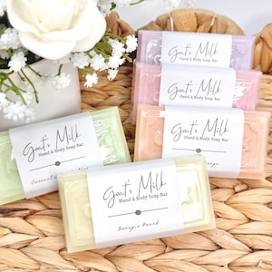 Puede incluir: Cuatro pastillas de jab&oacute;n rectangulares de leche de cabra para manos y cuerpo en tonos pastel verde, amarillo, rosa y lavanda. Cada pastilla est&aacute; envuelta en una banda de papel blanco con el texto Goat's Milk Hand & Body Soap Bar y aromas.