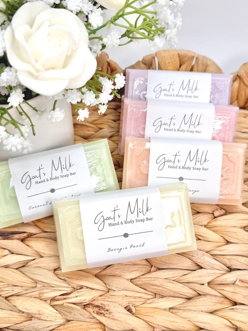 Puede incluir: Cuatro pastillas de jab&oacute;n rectangulares de leche de cabra para manos y cuerpo en tonos pastel verde, amarillo, rosa y lavanda. Cada pastilla est&aacute; envuelta en una banda de papel blanco con el texto Goat's Milk Hand & Body Soap Bar y aromas.