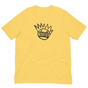 Puede incluir: Camiseta amarilla de manga corta con un gráfico en blanco y negro de una cara de dibujos animados con una corona de púas.