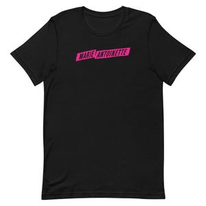 May include: Black short-sleeve t-shirt with the text "MARIE ANTOINETTE" in bright pink, displayed in a rectangular shape across the chest. The shirt is made of a soft material and has a classic crew neck.