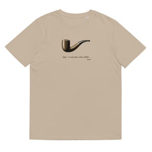 May include: A beige t-shirt with a black and brown pipe illustration and the text "Ceci n'est pas une pipe." in black.