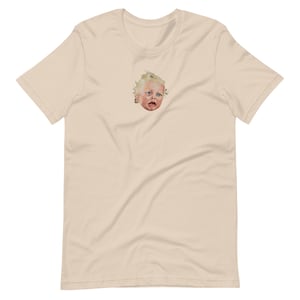 Pode incluir: Uma camiseta bege com um gráfico de um rosto de bebê chorando.