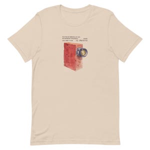 May include: A beige t-shirt with a red brick-like camera illustration and the text "Film vrai mérite un film de Satyricon révolutionnaire" and "LE PICROANE".