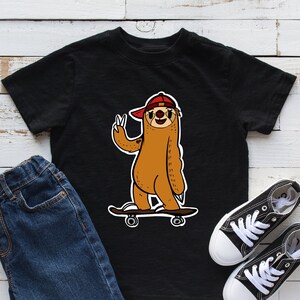May include: Black t-shirt with a cartoon illustration of a sloth wearing a red hat and skateboarding. The sloth is giving a peace sign with one hand and holding the skateboard with the other. The sloth is brown with a white belly and has a black outline. The skateboard is black with white wheels.