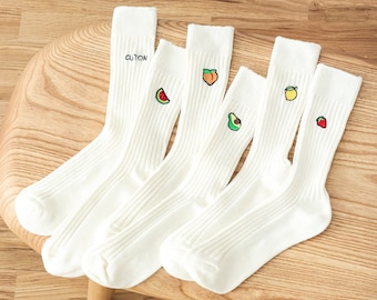 May include: Four pairs of white cotton socks with different fruit designs embroidered on them. The designs include a watermelon, a peach, an avocado, and a lemon. The socks are ribbed and have the word "CUTION" written on one of the socks.