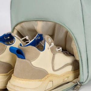 May include: A light blue duffel bag with a zipper closure. The bag is open and two pairs of off-white sneakers with blue accents are inside.