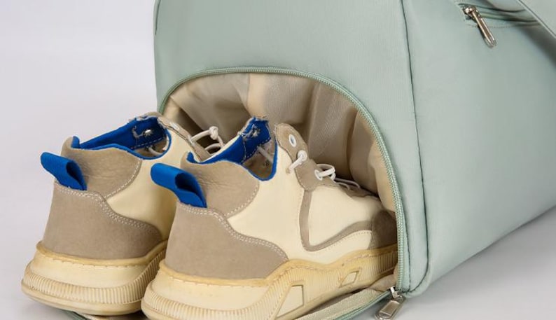 May include: A light blue duffel bag with a zipper closure. The bag is open and two pairs of off-white sneakers with blue accents are inside.