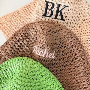 May include: Close-up of several woven hats in shades of beige, brown, and green. The top hat has the embroidered letters "BK" in black. The middle hat has the name "Rachel" embroidered in pink.