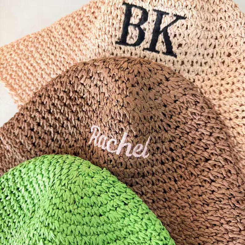 May include: Close-up of several woven hats in shades of beige, brown, and green. The top hat has the embroidered letters "BK" in black. The middle hat has the name "Rachel" embroidered in pink.