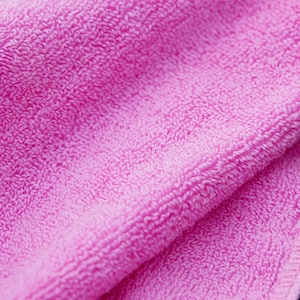 May include: Close-up of a folded, bright pink terry cloth towel. The soft, textured surface of the towel is visible, with a detailed view of the looped fibres. The edges of the towel are neatly finished.