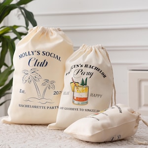 Puede incluir: Tres bolsas con cordón de color crema con texto e ilustraciones impresos. La bolsa más grande dice "Molly's Social Club" con palmeras. La bolsa del medio dice "Frances's Bachelor Party" con un cóctel. La bolsa más pequeña también tiene texto.