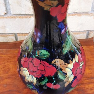 Può includere: Un vaso in ceramica nera con un'ampia apertura e un corpo rotondo. Il vaso è decorato con motivi floreali rossi, dorati e verdi.