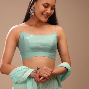 May include: A light teal crop top with thin straps, paired with matching trousers featuring a gold pattern. The outfit is complemented by a matching scarf and silver earrings. The text "Balaji Boutique" is visible on the top.